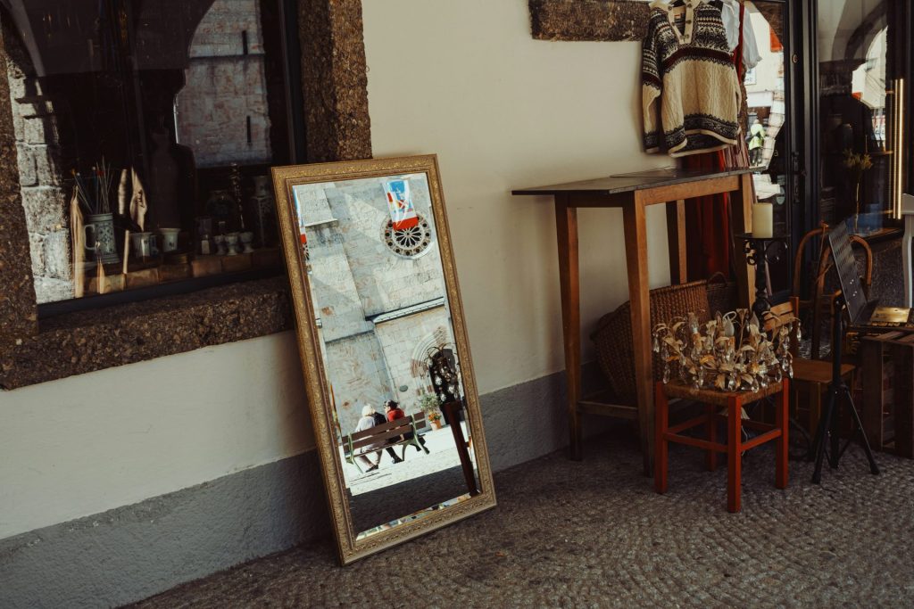 A room with a chair, table, mirror and pictures on the wall